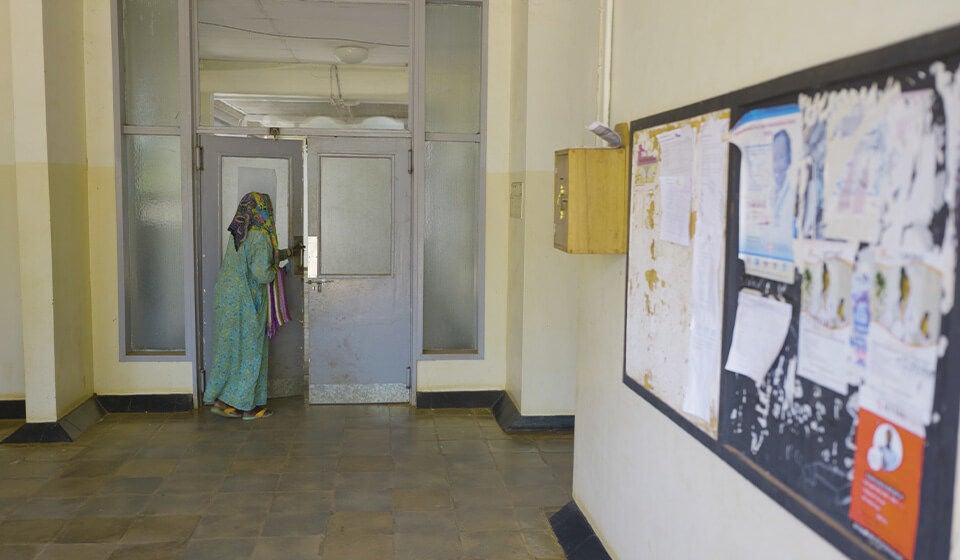 A women holding a bag, begins to open a door at the far end of the room.