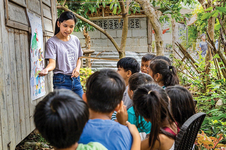A young woman tells a group of children a story in a garden. (Philippines, 2024)