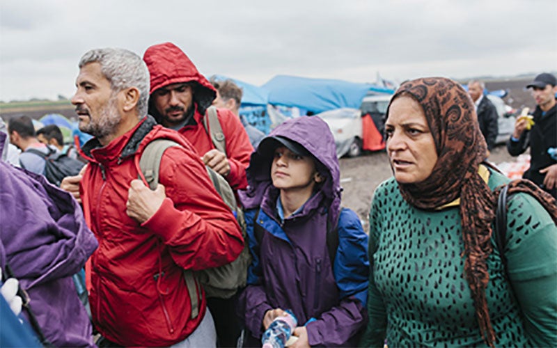 A group of people from Syria stand expectantly, waiting for a bus to take them to safety elsewhere.