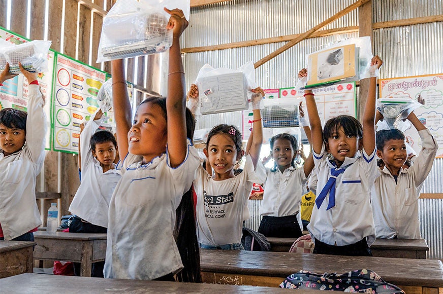 A classroom of young students participate in a fun activity that involves raising their arms above their heads. (Cambodia, 2024)