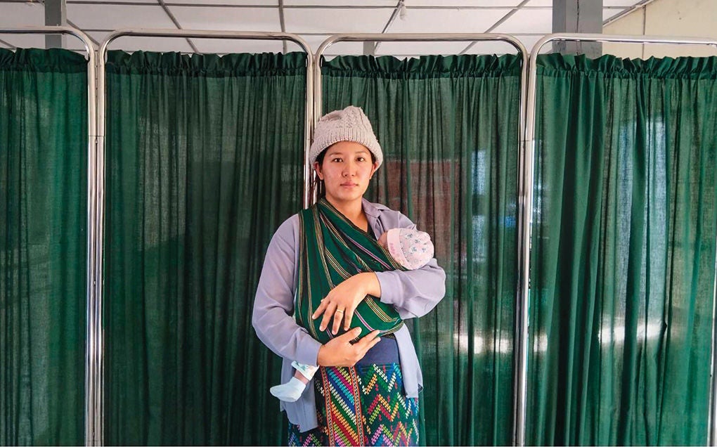 A mother carrying her baby in front of a hospital ward.