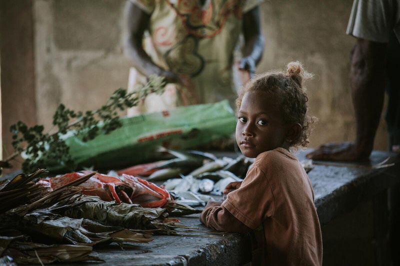 A young child looks toward camera looking solemn, beside a table with a few shellfish.