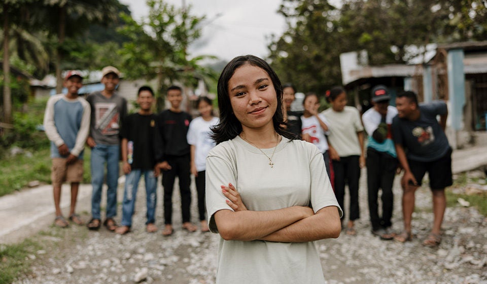 A girl in a white shirt, crosses her arms and smiles. (Indonesia, 2023)
