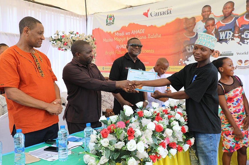 A man wearing a brown long sleeve awards an adolescent male wearing a black t-shirt a certificate.
