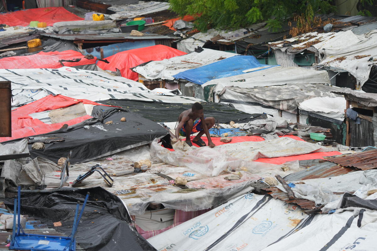 Man securing tarps on top of his shelter in Camp Domond. 