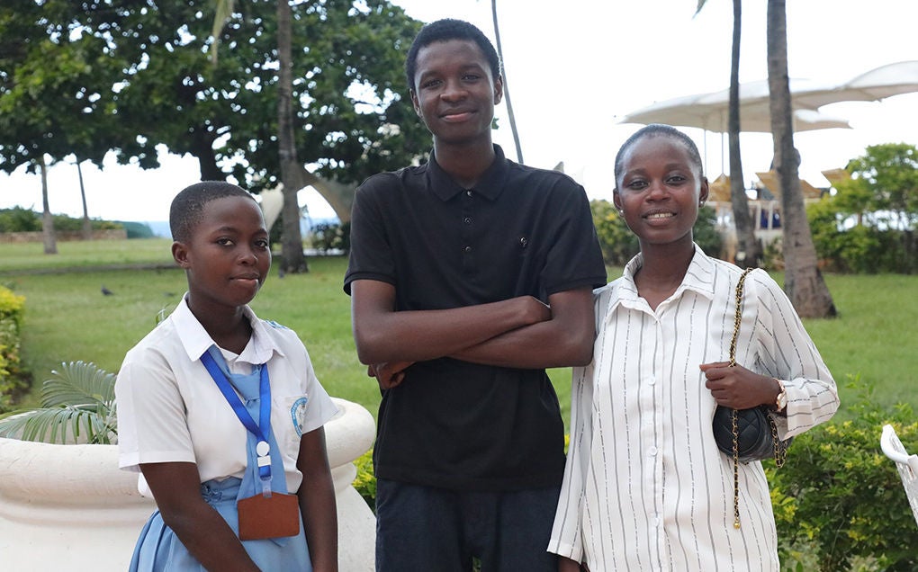 Two adolescent girls and one adolescent boy stand together and smile.