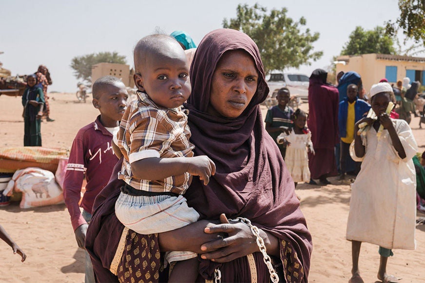 A mother holds a young child while standing among other families at the Sudan-Chad border.