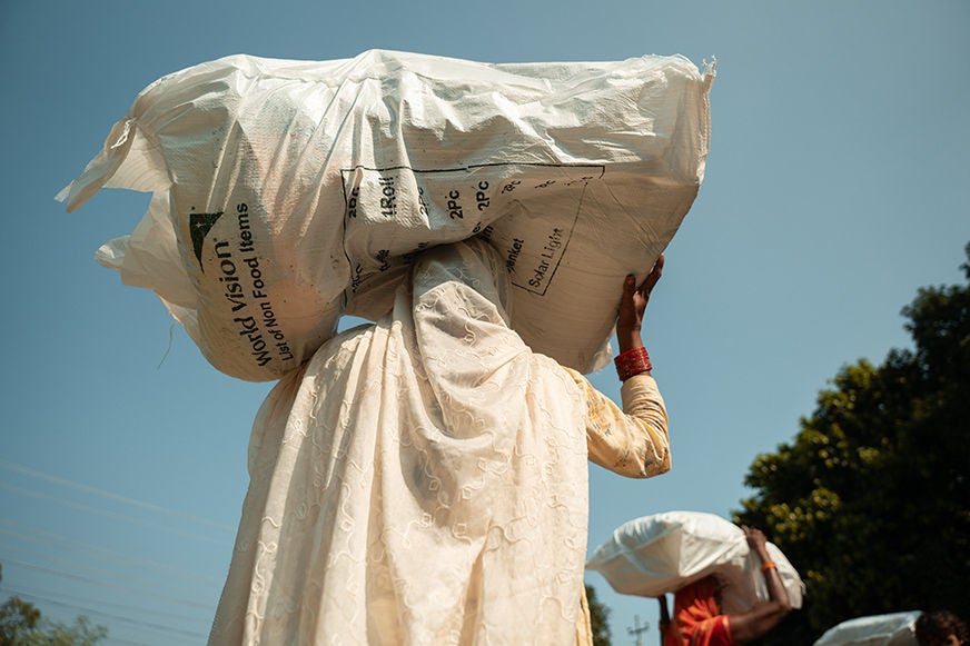 Woman in light coloured head scarf balances huge bag on her head. 