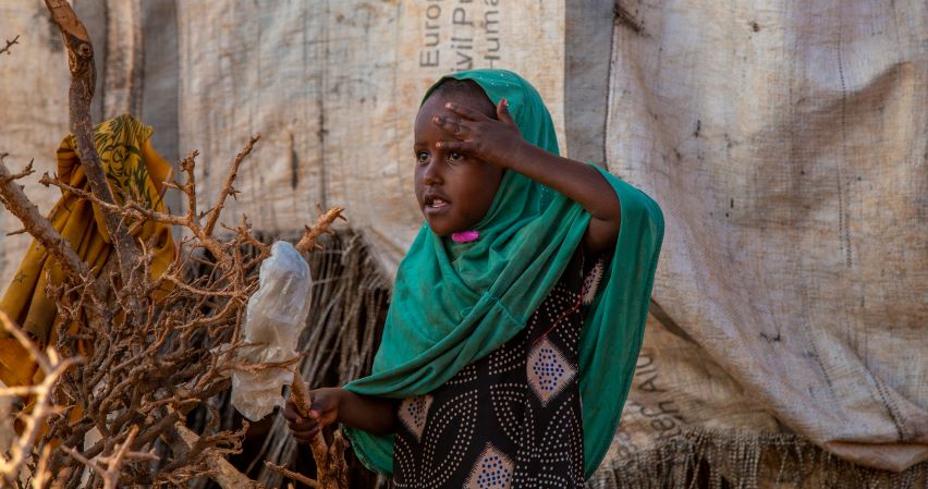 A young girl shades her eyes as she looks across the camp. Somalia, 2023