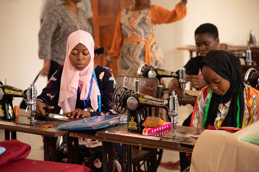 Two adolescent girls use sewing machines.
