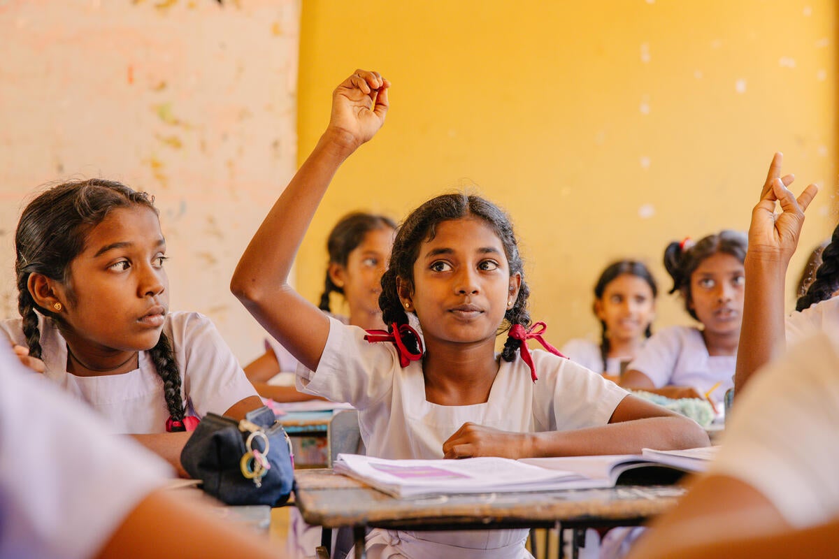 A schoolgirl with twin braids raises her hand to answer a question. (Sri Lanka, 2025)