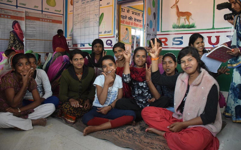 A group of teen girls are sitting on the floor.