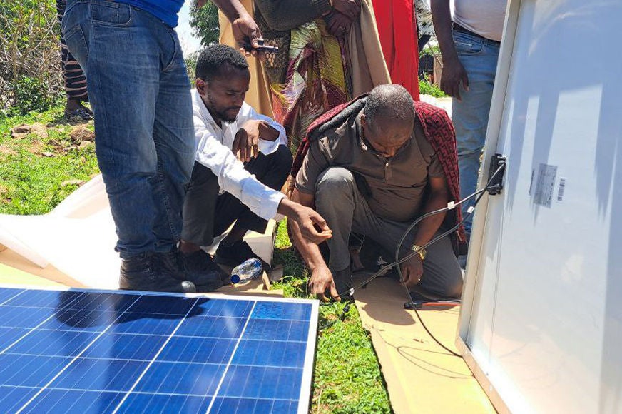 A team of people work together to install solar panels on the ground in a lush, green environment.