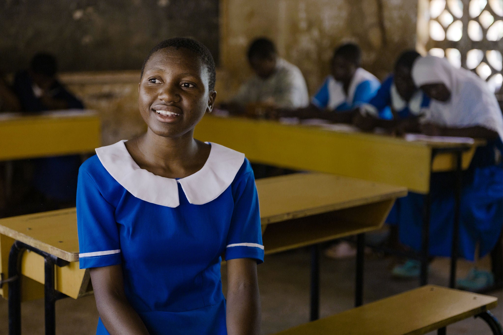 Teenage girl sits at a desk, smiling.