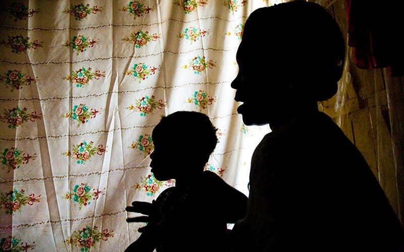 A silhouette of a women and girl in front of a flowered bedsheet hanging in the background.