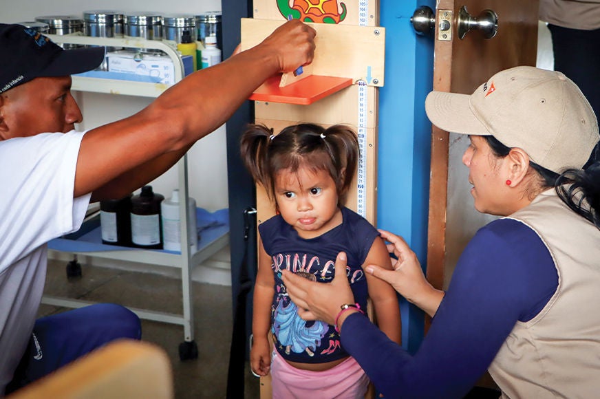 World Vision community health workers measure the height of a little girl during a check-up. (Venezuela, 2024)