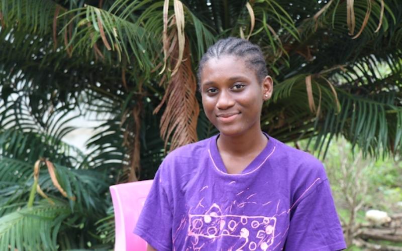 Tenema in Sierra Leone stands in front of palm trees.