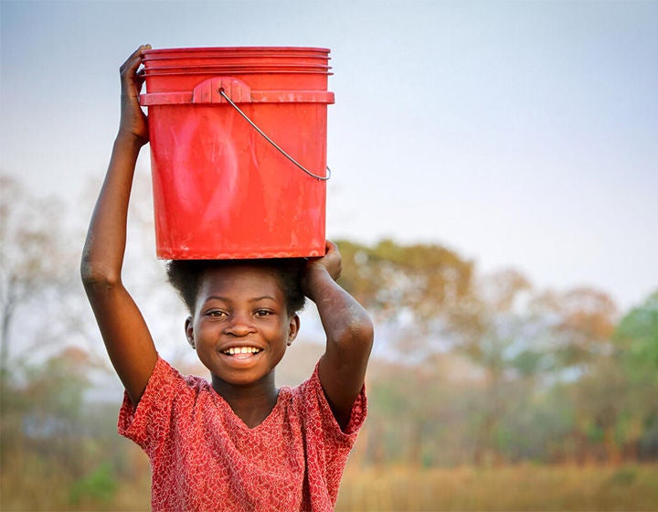 A child smiling as she holds a bucket over her head.