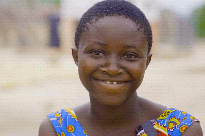 A young girl in a blue patterned shirt, smiles. (Ghana, 2024).