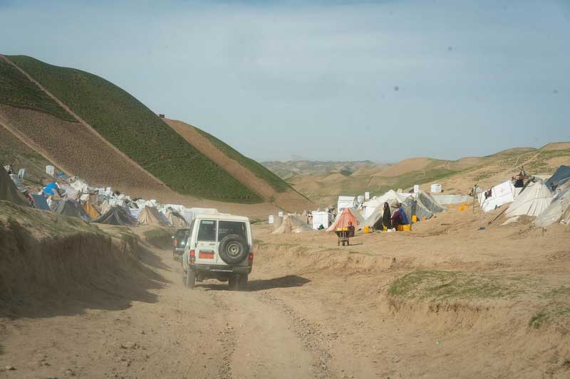 A car drives down a dusty road in a dry region of Afghanistan.