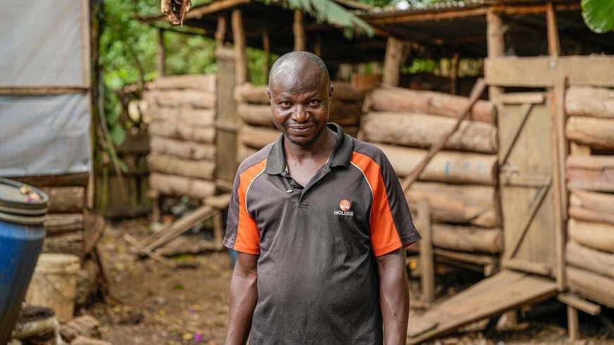 A man in a tropical setting looks toward the camera with a resolute expression.