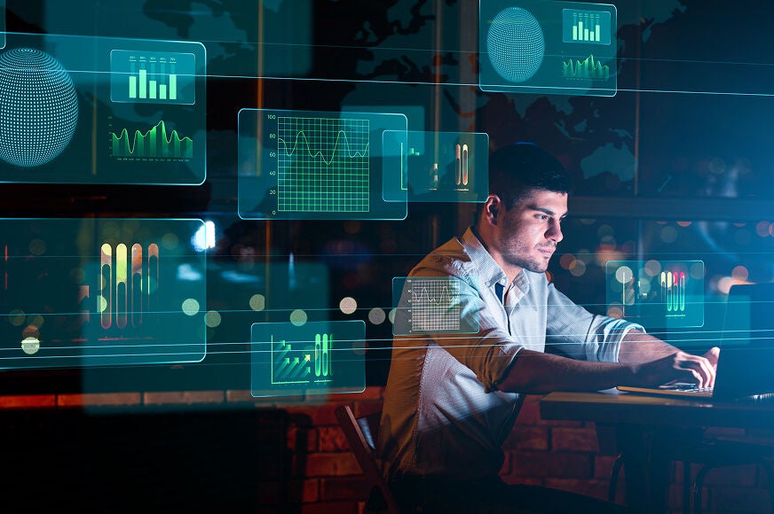 A man using a laptop with various glowing digital data visualizations and global maps overlaid in the air.