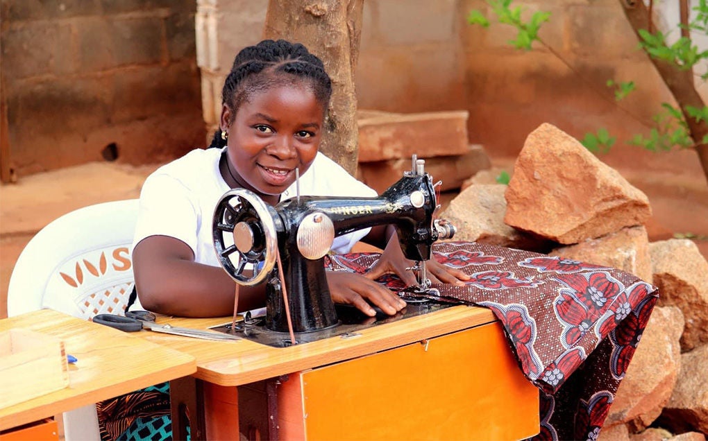 A girl smiles while sewing.