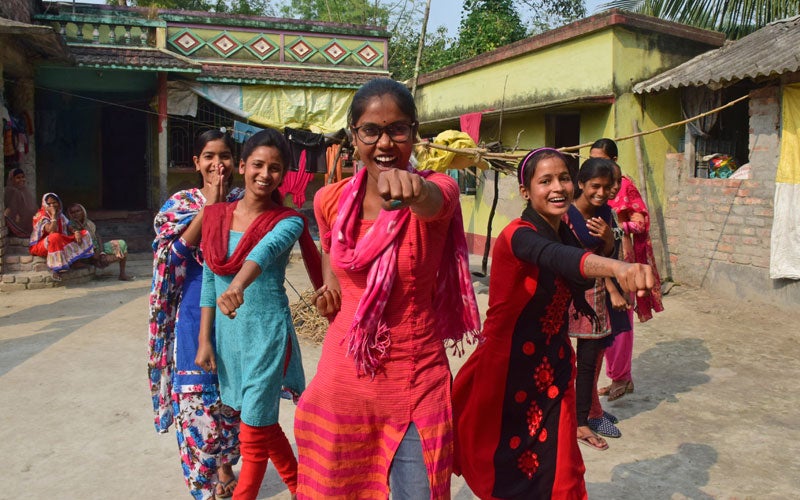  A group of smiling Indian girls stand in a 'V' formation with fists out.