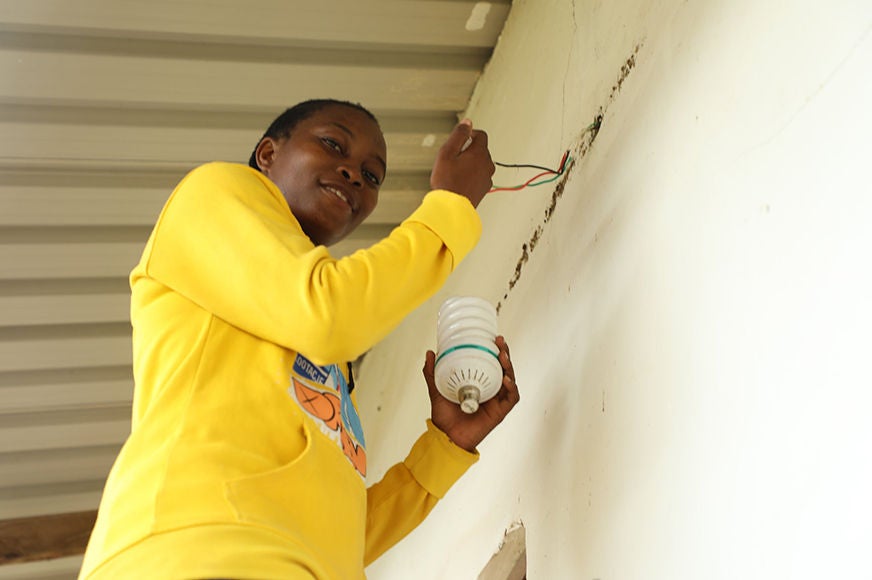 An adolescent girl wearing a yellow shirt fixes a lightbulb.