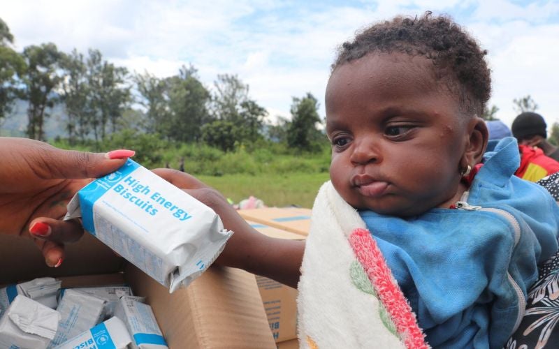 A toddler looks at the pack of high-energy biscuits being passed to her.