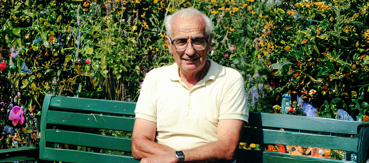 Elderly person in a yellow shirt sitting on a green bench in a colorful garden.