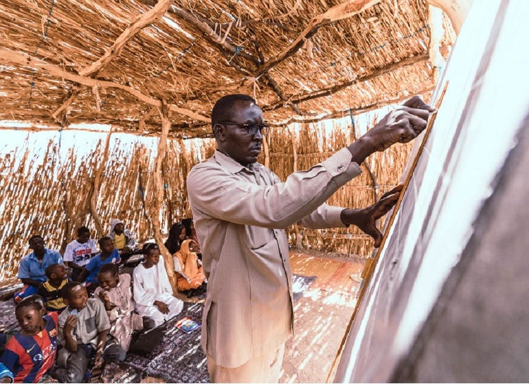 A teacher stands at a chalkboard while students look at him.