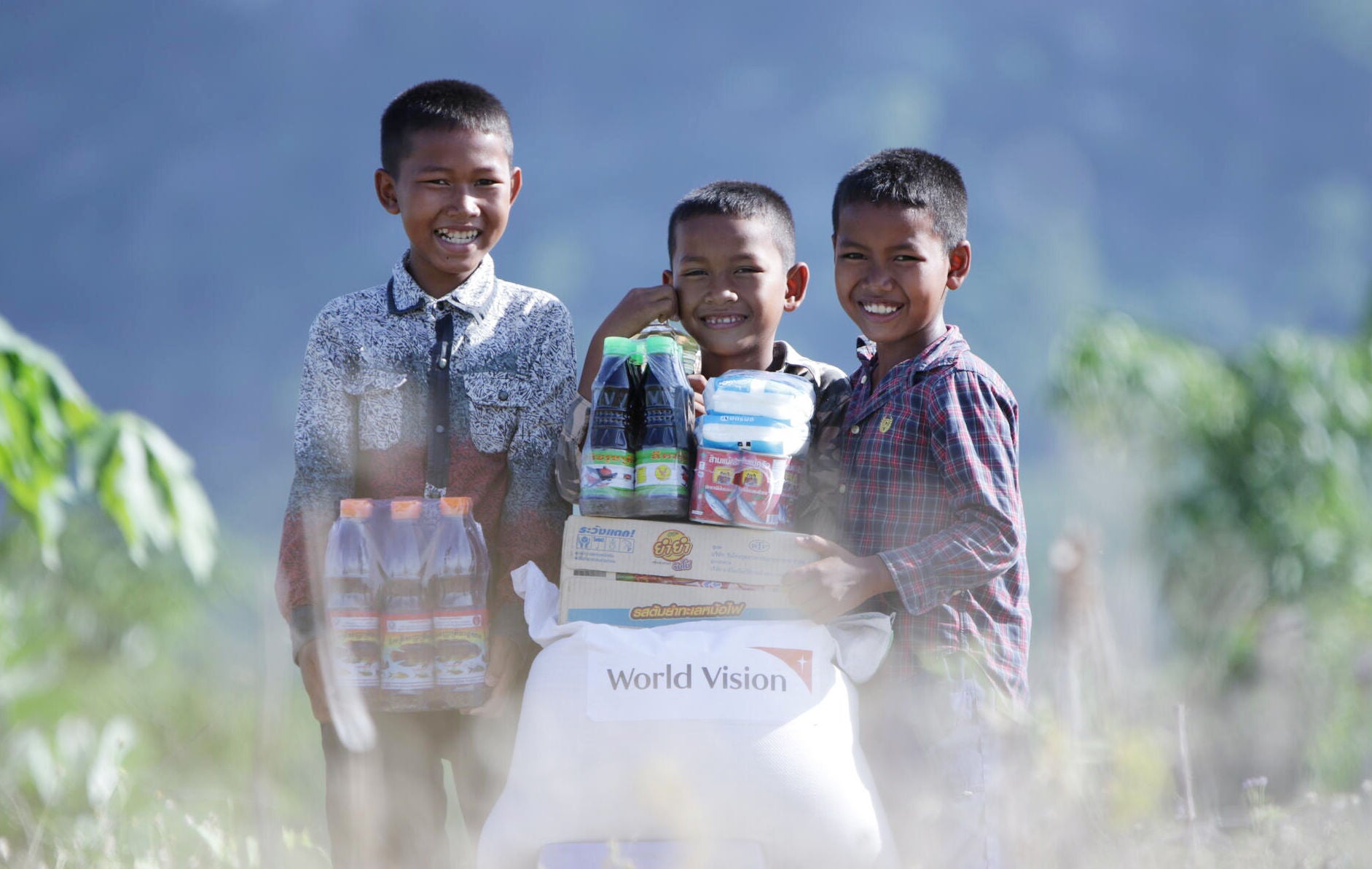 Three boys are smilling while holding unto their food basket items provided by World Vision.