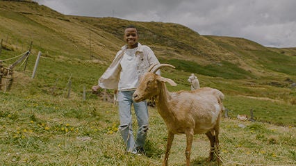 Young boy dances with goat in a field.