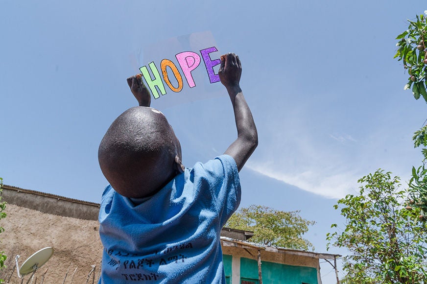 A young boy holds a handwritten sign up to the sky that reads, “hope.” (Ethiopia, 2025)