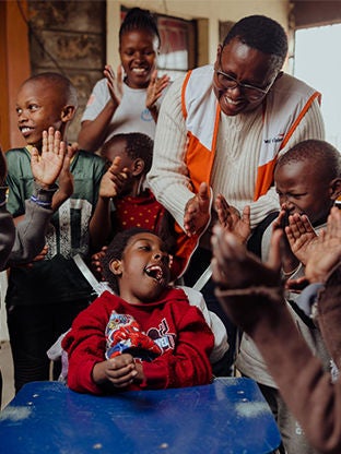 A World Vision staff member and children are clapping together.