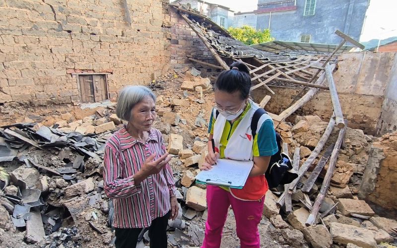 A World Vision worker speaks to a woman affected by a disaster in front of rubble