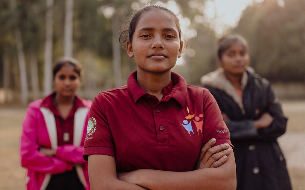 Neha (centre) stands confidently with two teenage girls, their arms crossed.