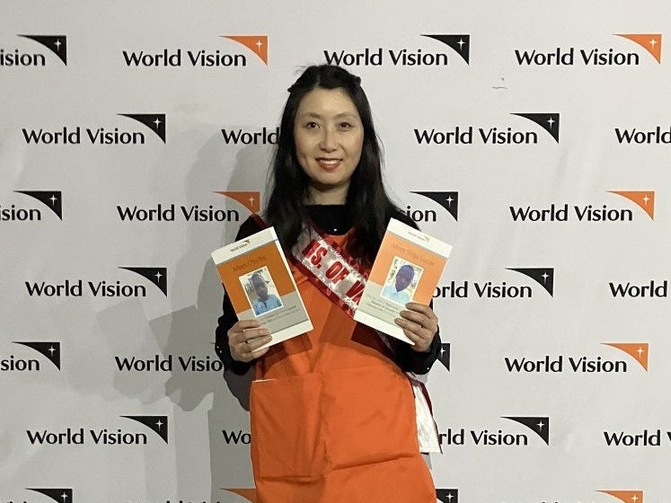 A woman in an orange apron holds pictures of two children available for sponsorship with World Vision.