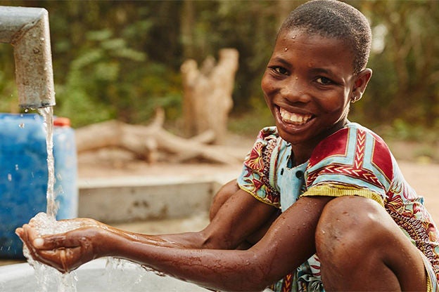 A girl smiles as she holds her hands under a water tap.
