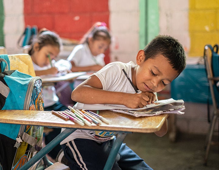 A young boy sitting on his chair drawing on paper.