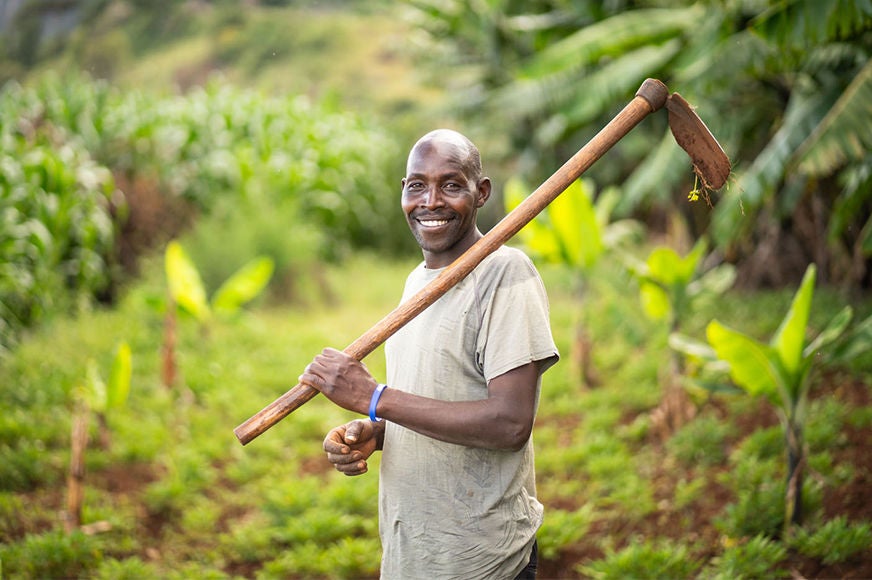 A man smiles with a farming tool.