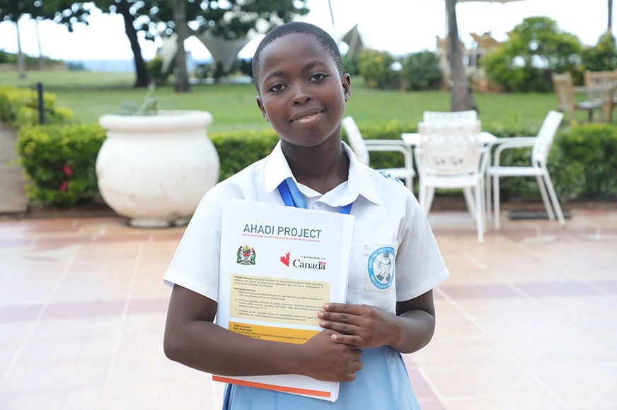 An adolescent smiles and holds a stack of papers.