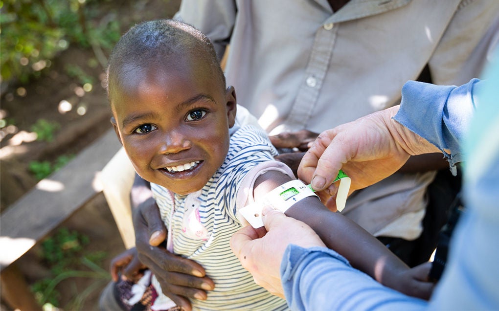 A child smiles while having their arm circumference measured.