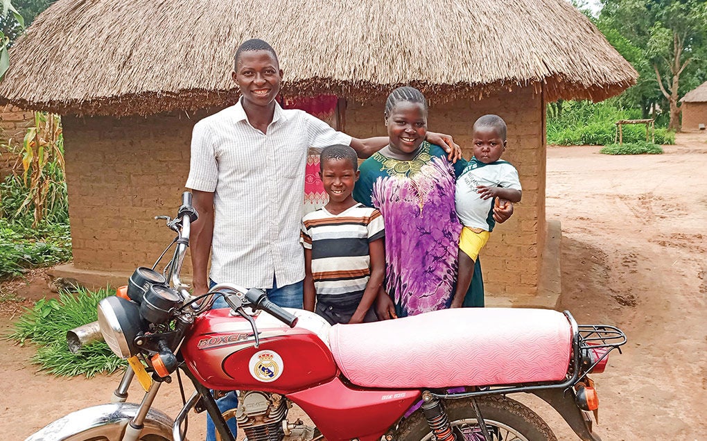 Family of four stands behind a red motorcycle outside their home in South Sudan.