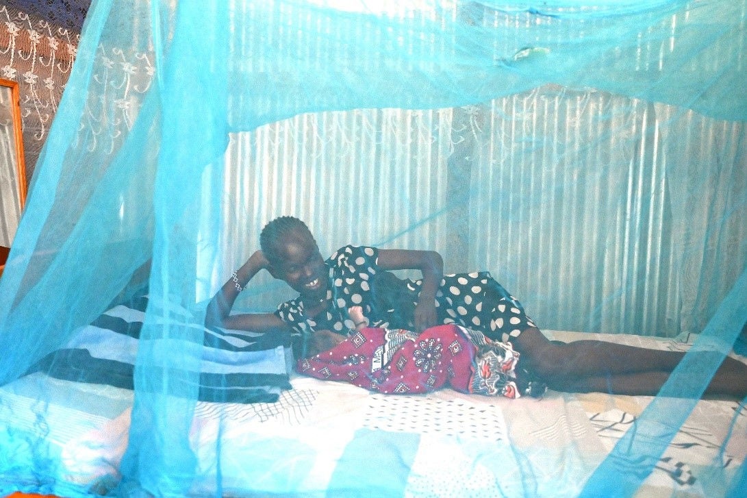 In Turkana County, Kenya, a new mom practices side-lying breastfeeding with her infant under a blue mosquito net.
