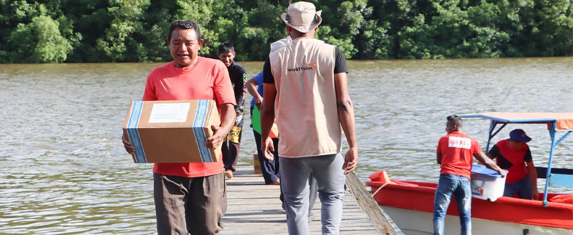 World Vision staff walk along dock carrying boxes. (Venezuela, 2024)