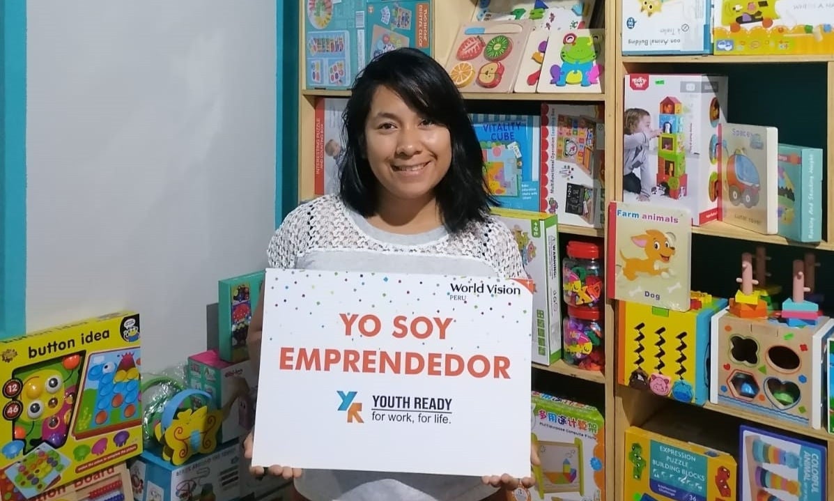 In Peru, a woman stands in front of a toy display holding a sign in Spanish that translates to ‘I am an entrepreneur.’  