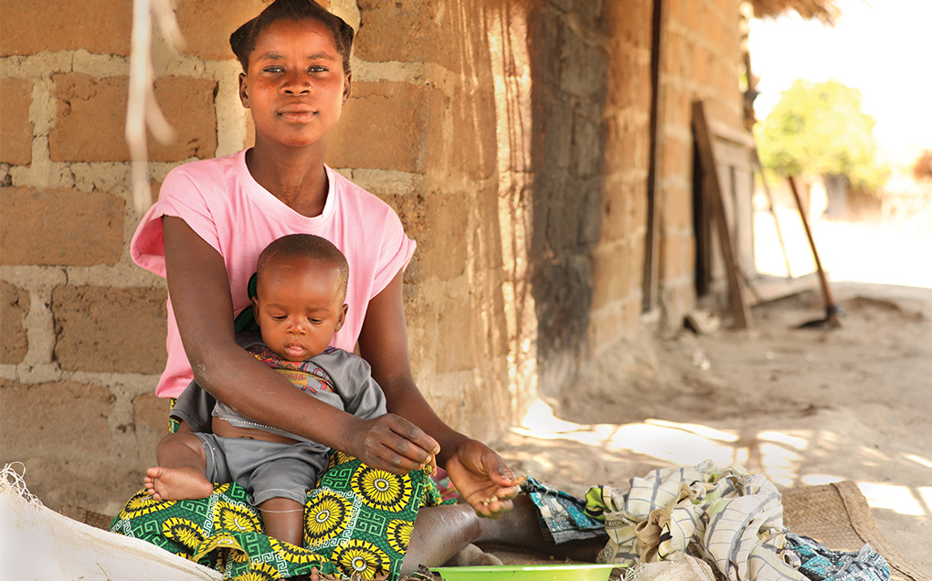 A young woman in a pink shirt, sits, holding small a child.