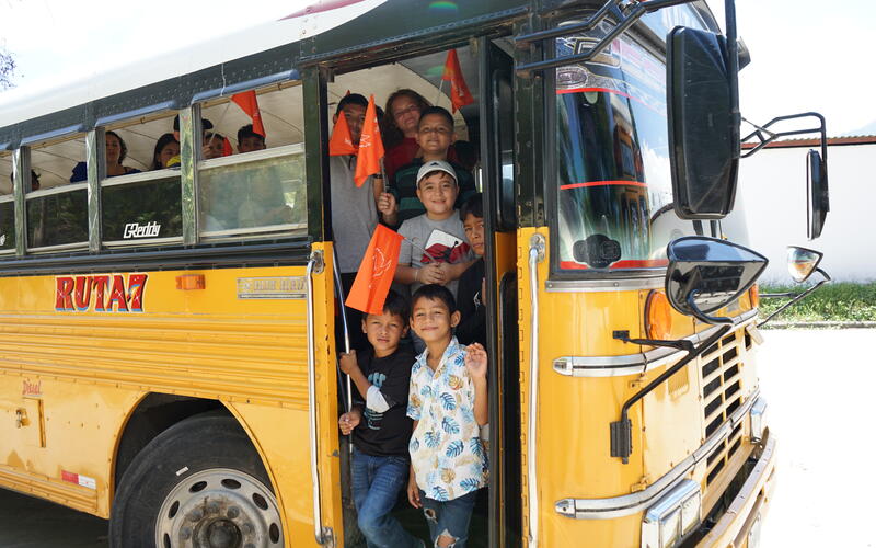 In Honduras, a group of children holding orange flags smile sand prepare to exit a school bus
